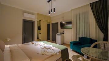 A hotel room with a bed, a sofa, a small table, a TV, and an air conditioning unit.