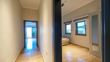 A modern, well-lit hallway leading to a bedroom with a large window, a door, and a visible balcony.