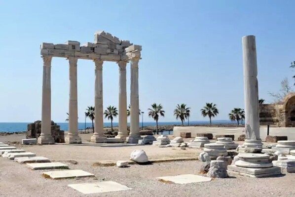 Ancient ruins with columns and stone steps, located near a beach with palm trees and the sea in the background. - Eden Nest Exclusive (Serik)