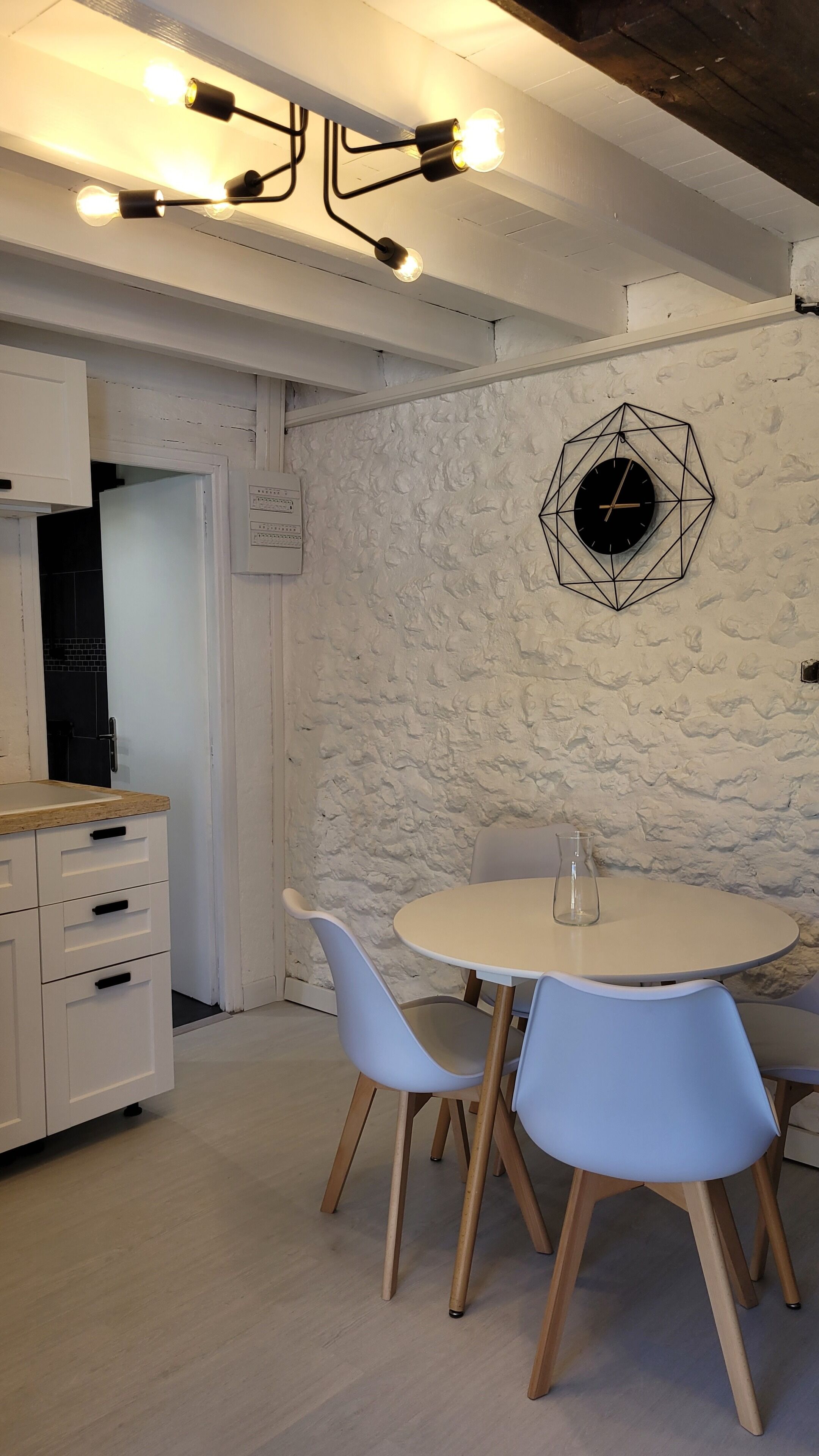 A modern kitchen with white cabinets, a round table with chairs, and a geometric wall clock.