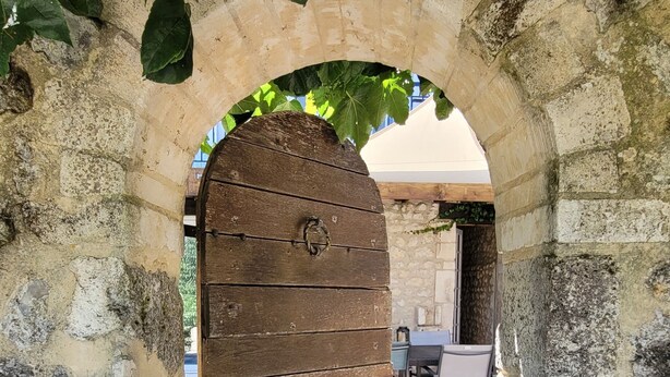 Un arcoado acceso de piedra con una puerta de madera, que conduce a un espacio al aire libre con mesas y sillas.