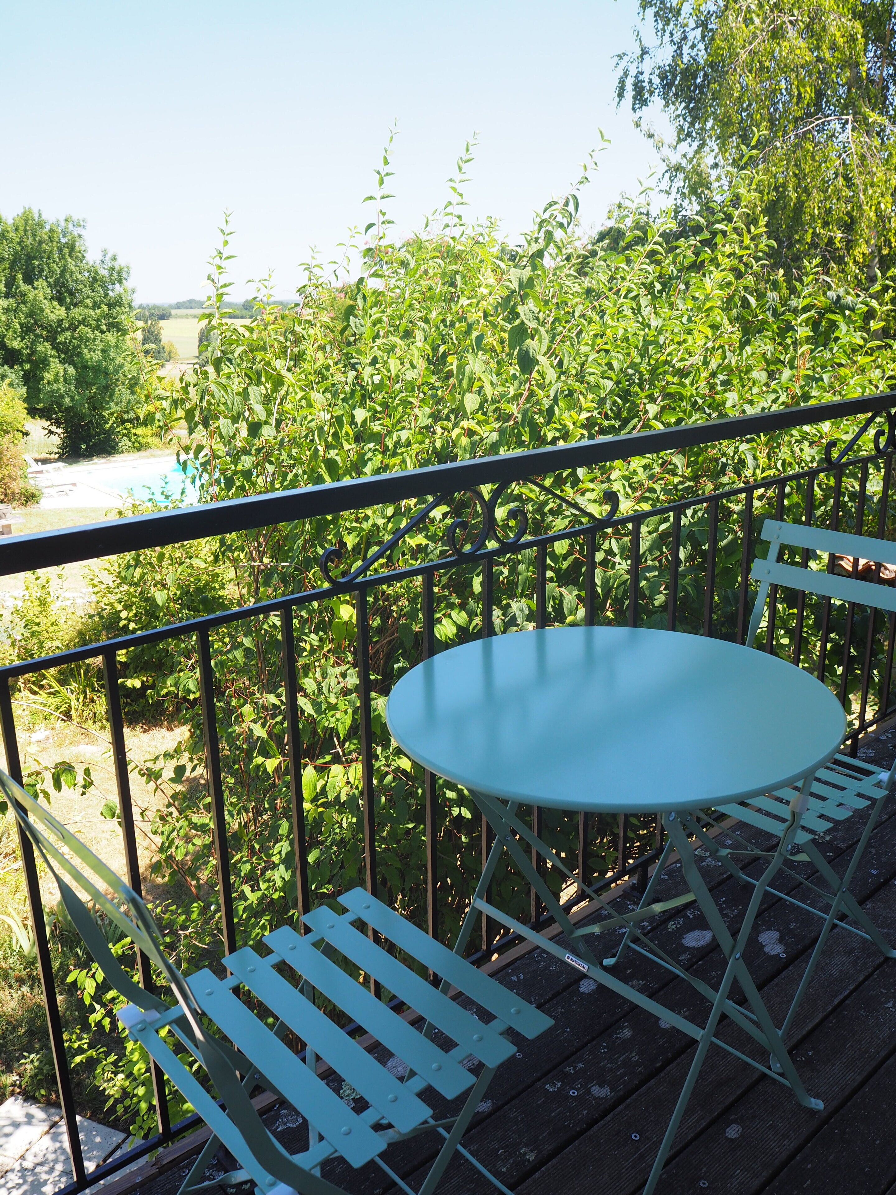 A balcony with a round table and two white chairs, surrounded by a metal railing.