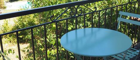 A balcony with a round table and two white chairs, surrounded by a metal railing.