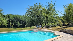 Una piscina con borde de piedra, rodeada por un muro de piedra y una zona ajardinada.