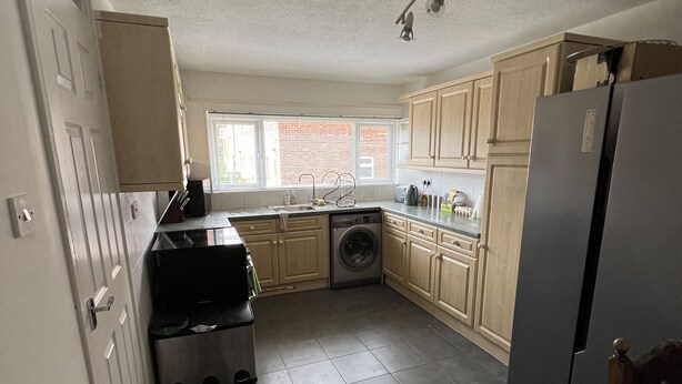 A compact kitchen with a washing machine, a refrigerator, and wooden cabinets. - Fellowes Garden (Peterborough)