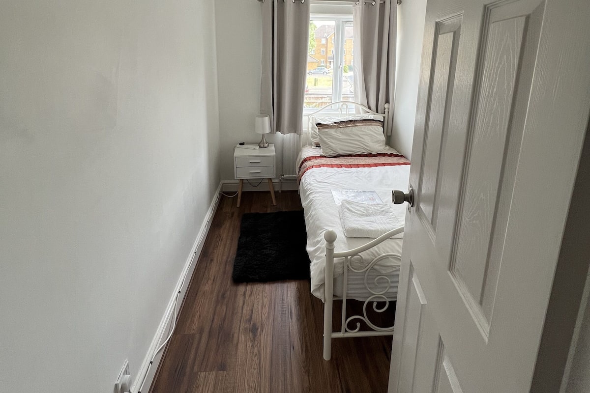 A bedroom with a bed, bedside table, lamp, and a window with curtains.