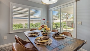 A dining area with a wooden table, chairs, a vase of flowers, and a ceiling light fixture.