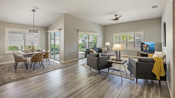 A spacious living room with a dining area, large windows, and a ceiling fan.