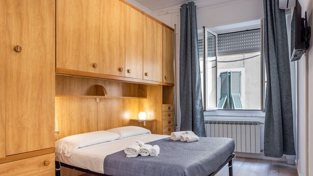 Ein Schlafzimmer mit Bett, Holzschrank, Fenster mit Rollläden und Heizkörper.