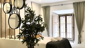 A bedroom with a bed, a potted plant, a mirror, and a window with curtains.
