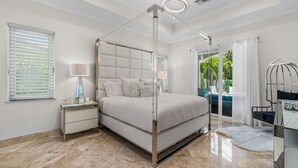 A modern bedroom with a four-poster bed, a nightstand, a lamp, and a view of the outdoors. - BY THE SEA VACATION VILLAS 5 STAR AQUABELLA  5/4 PRIVATE POOL WALK TO BEACH (Fort Lauderdale)
