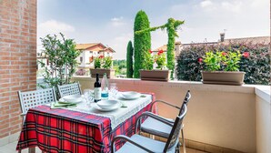 A terrace with a table set for two, potted plants, and a view of the surrounding buildings. - Borgo Tabari Appartamento Renoir (Mussolente)