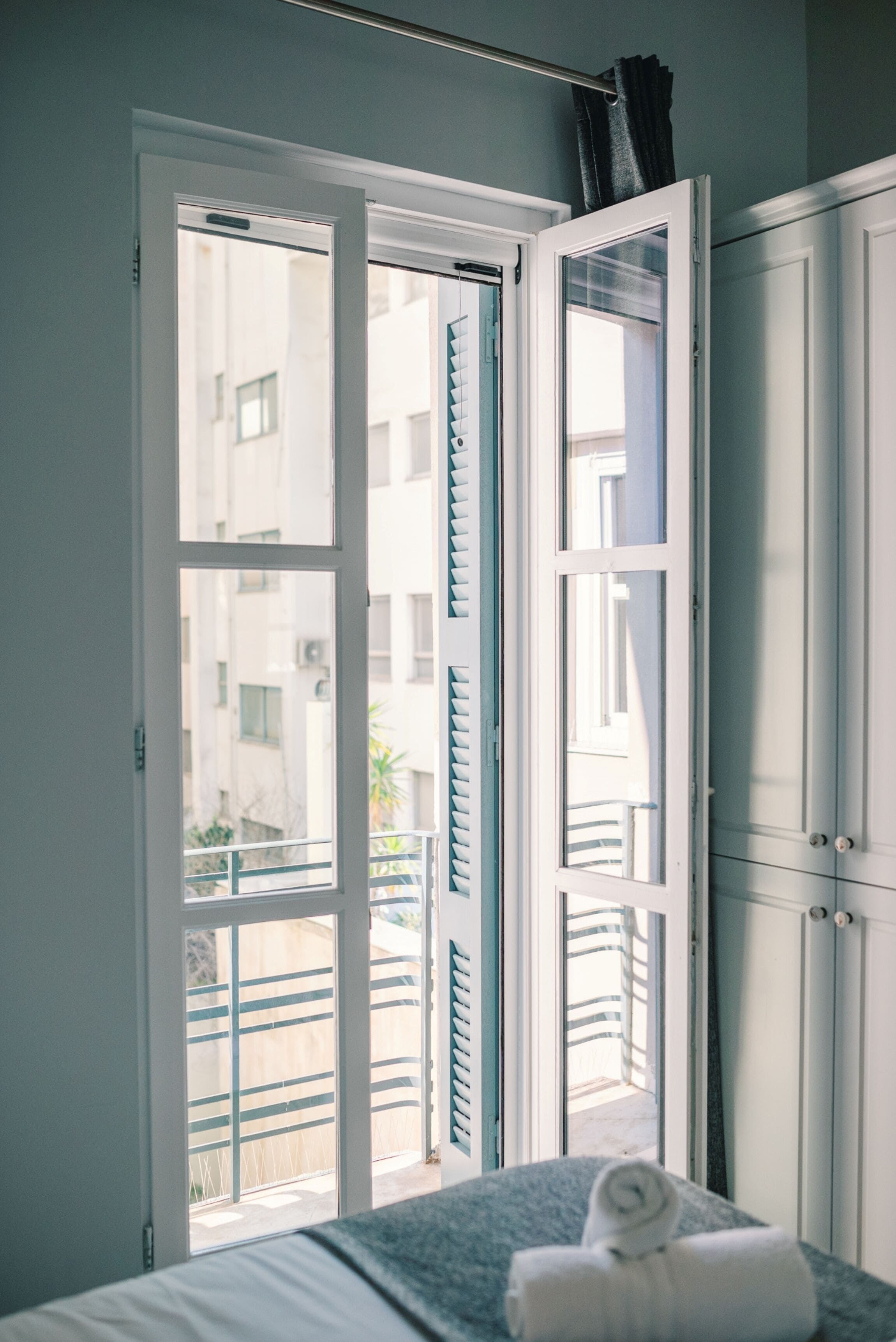A room with a bed, a window with a view of buildings, and a door.