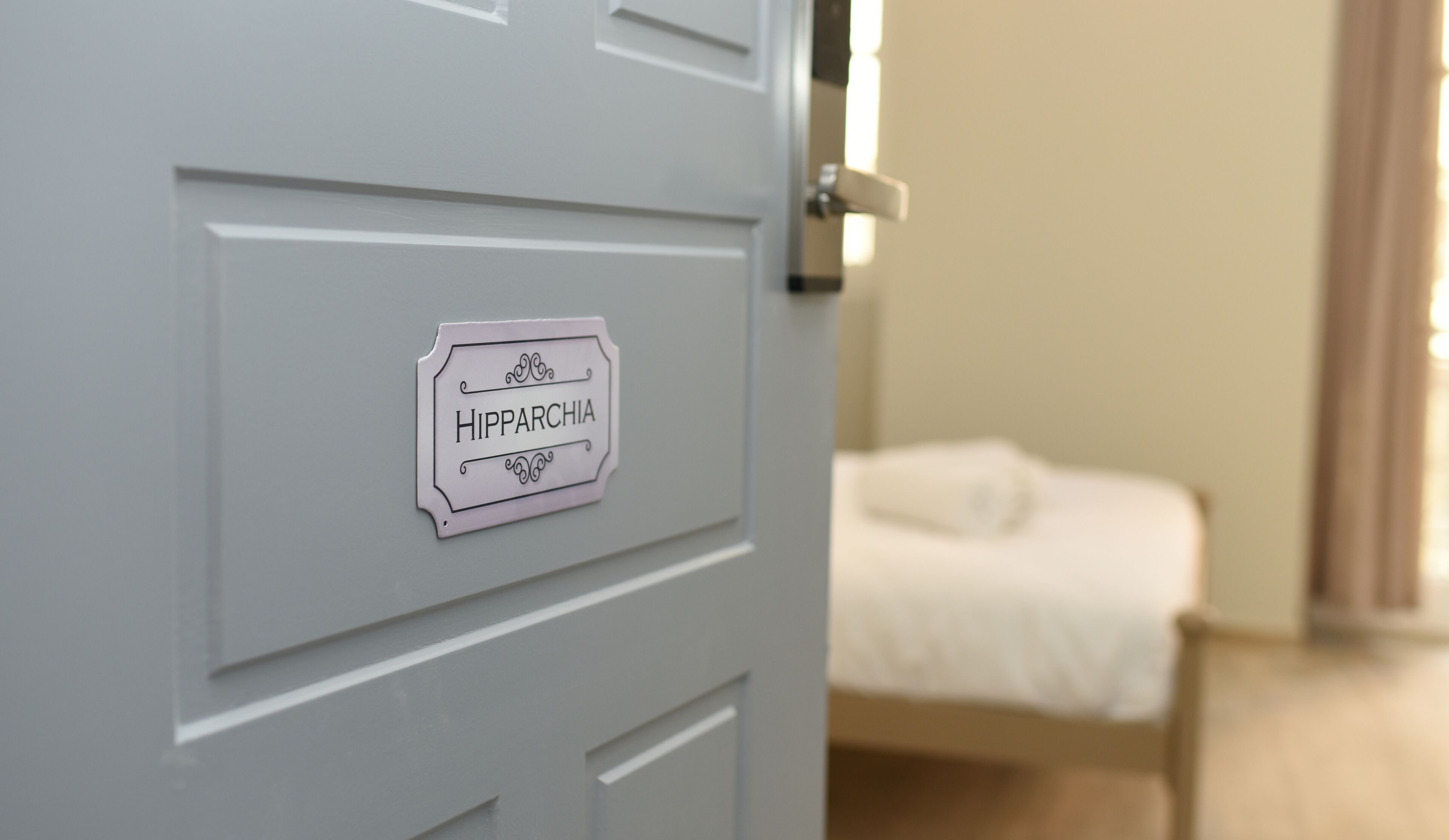 A door with a sign labeled "HIPPARCHIA" and a bed in the background.