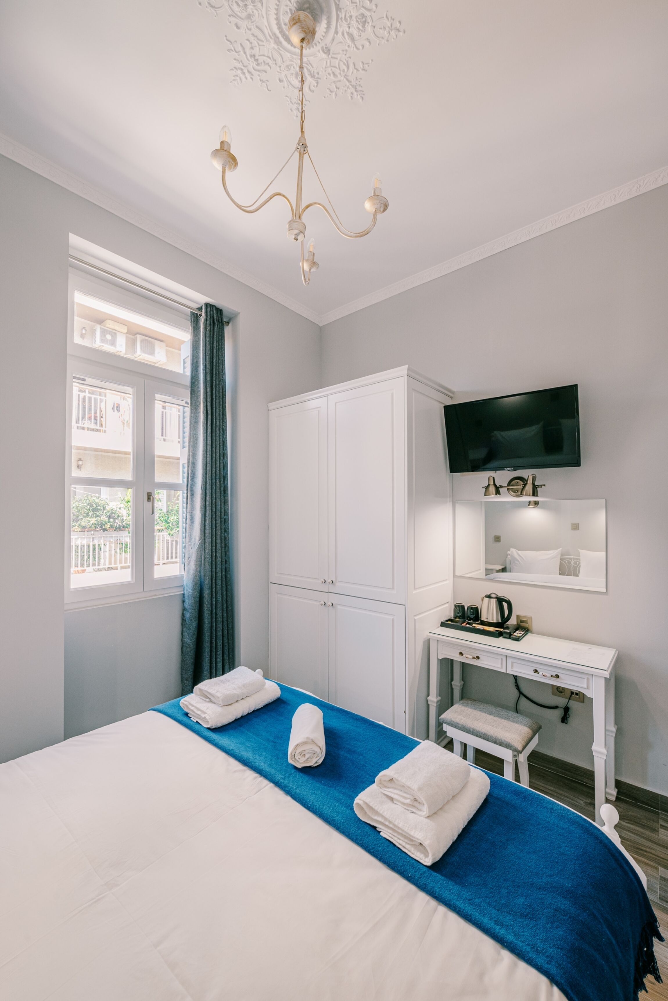 Een hotelkamer met een bed, een bureau met een flatscreen televisie, een kroonluchter en een raam met gordijnen.