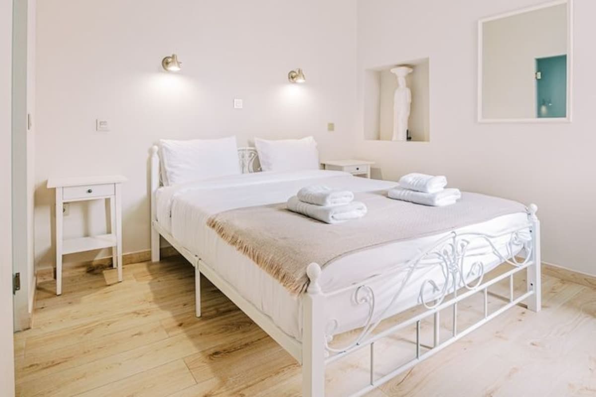 A bedroom with a white metal bed frame, a bedside table, a wall-mounted mirror, and a chandelier.