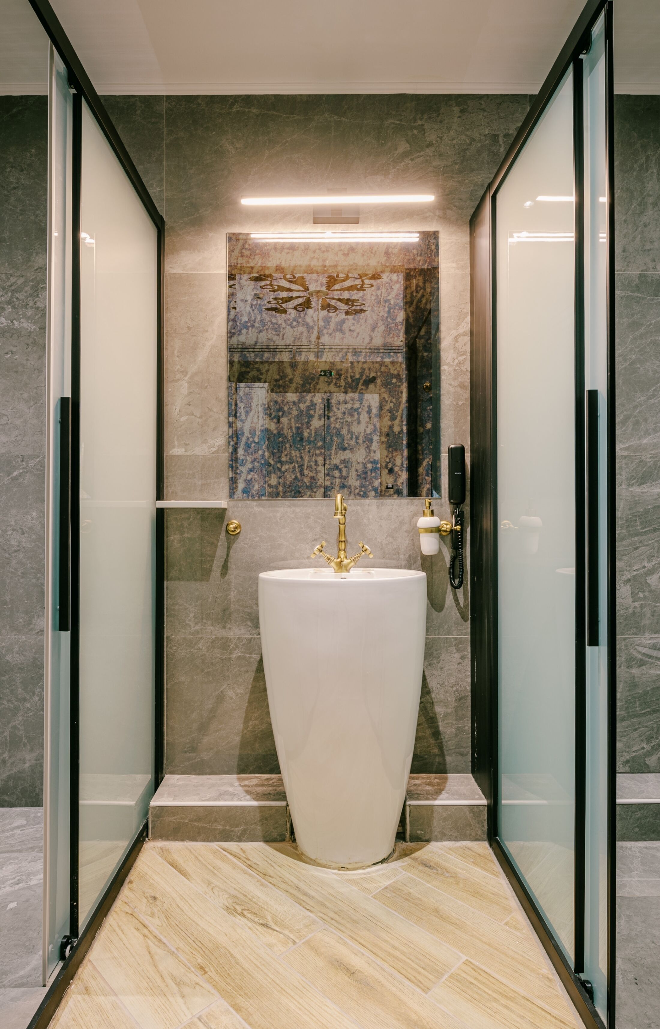 A modern bathroom with a large white sink, a glass-enclosed shower, and marble walls.