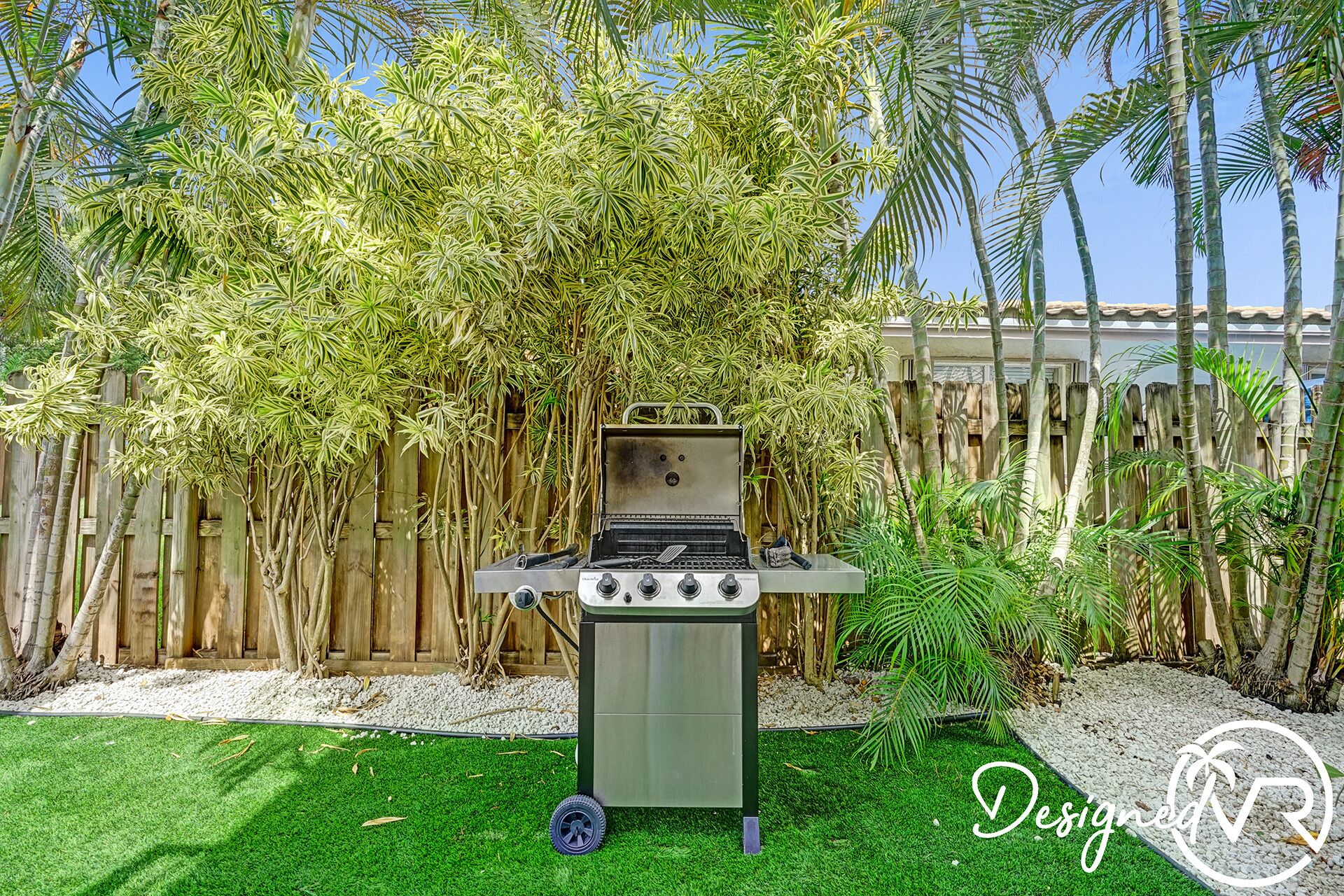 Una parrilla en un patio trasero con valla de madera y palmeras.