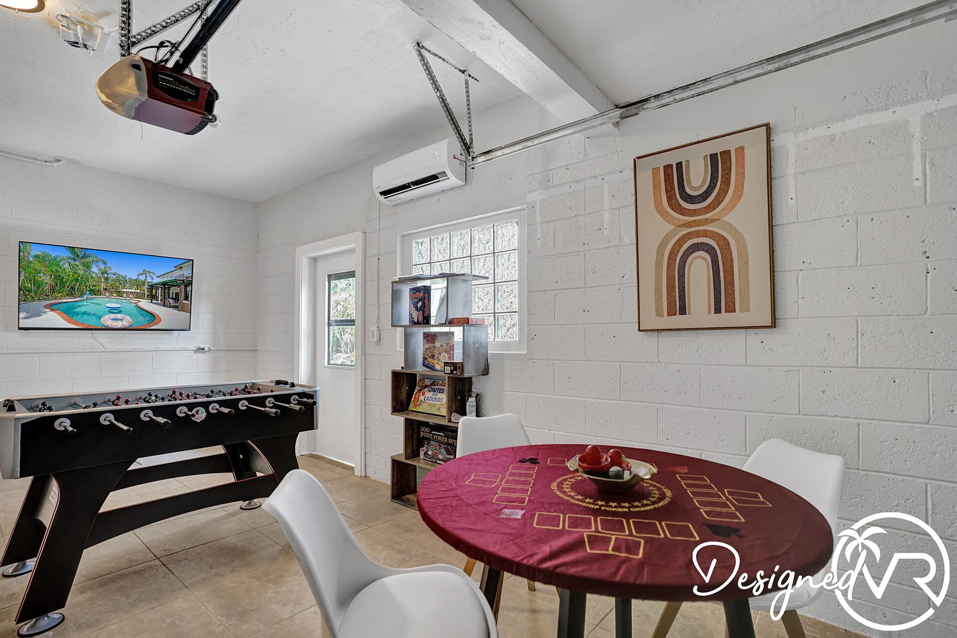 A room with a foosball table, a poker table, a projector, and a large painting on the wall.
