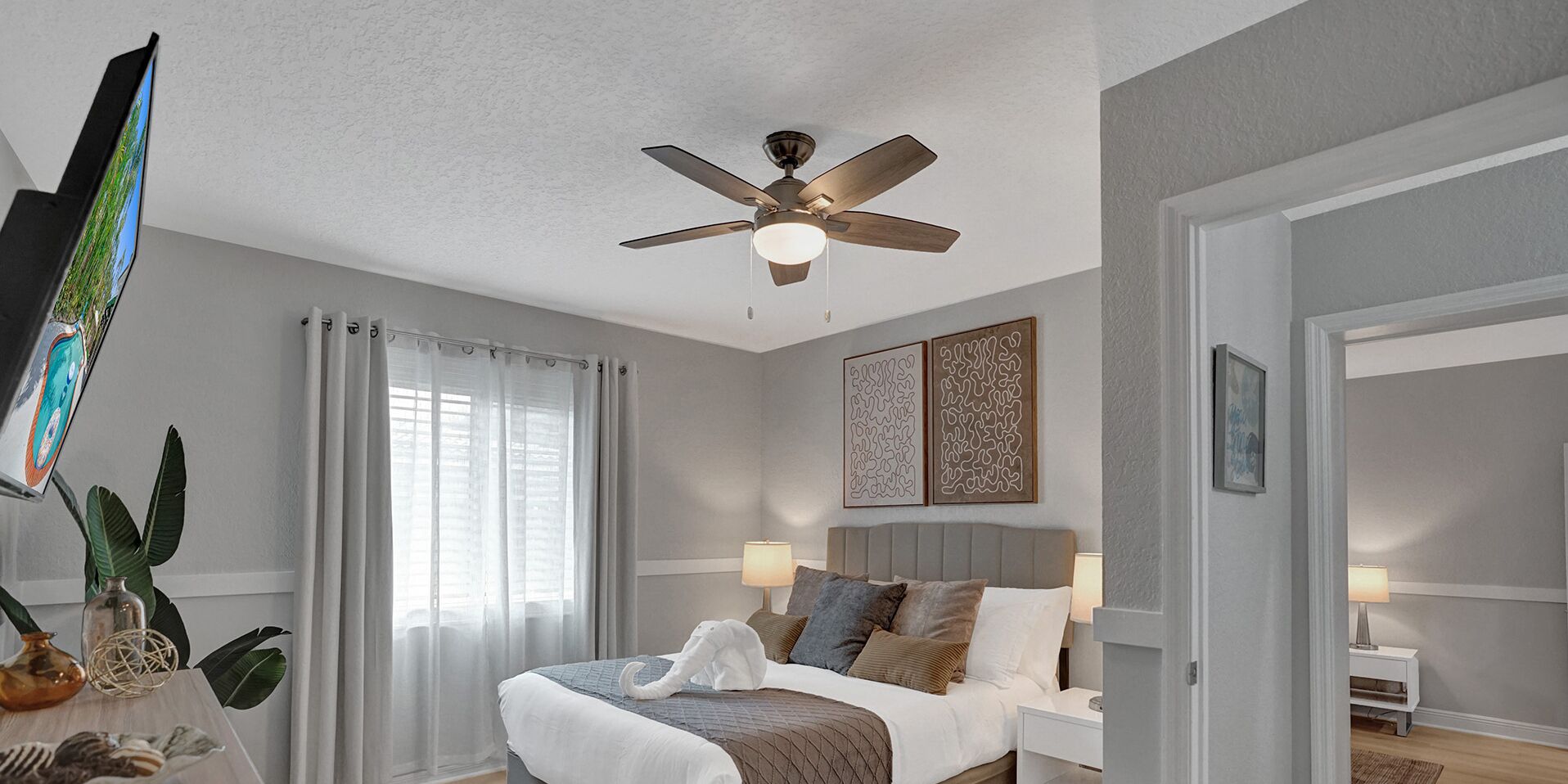 A bedroom with a bed, bedside tables, a ceiling fan, and artwork on the walls.