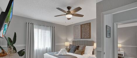A bedroom with a bed, bedside tables, a ceiling fan, and artwork on the walls.