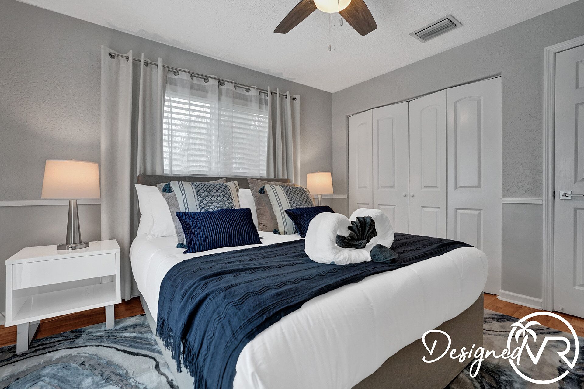 A bedroom with a bed, nightstands, a ceiling fan, a window with curtains, and a wardrobe.