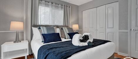 A bedroom with a bed, nightstands, a ceiling fan, a window with curtains, and a wardrobe.