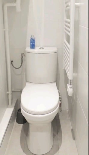 A compact bathroom with a toilet, towel rack, and trash bin.