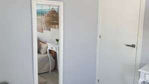 Una habitación con una puerta blanca, un espejo grande, una mesita pequeña y una silla gris.