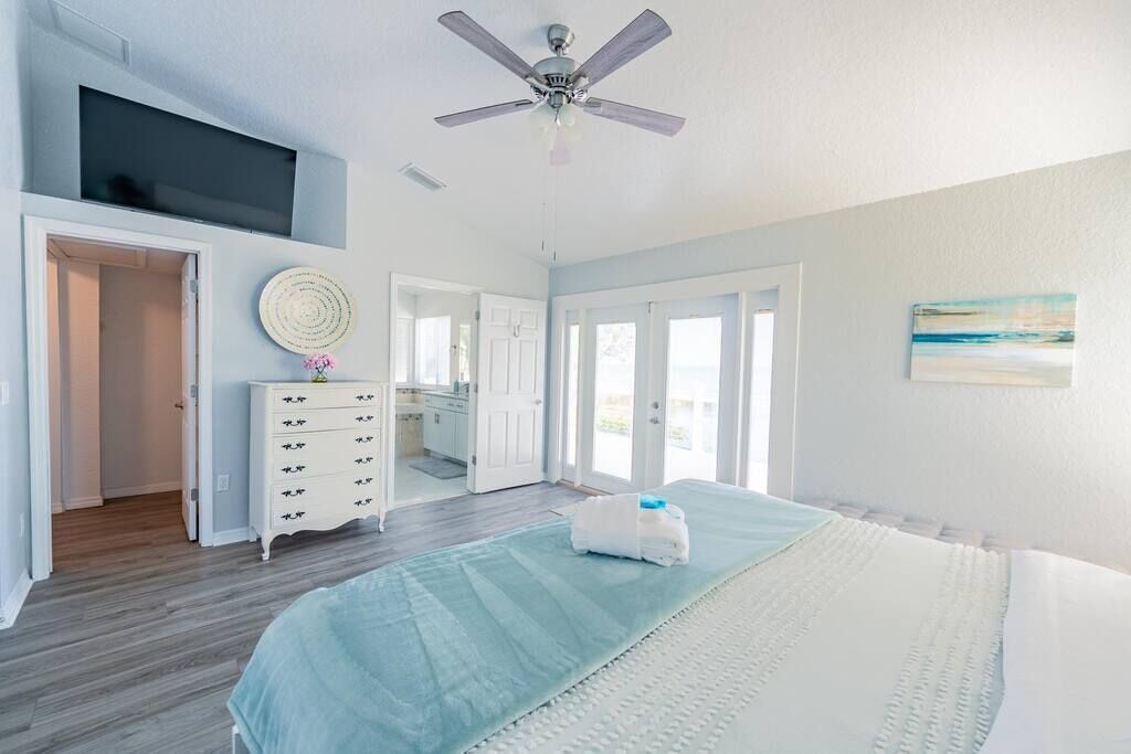 A bedroom with a bed, a ceiling fan, a dresser, and a TV mounted on the wall.