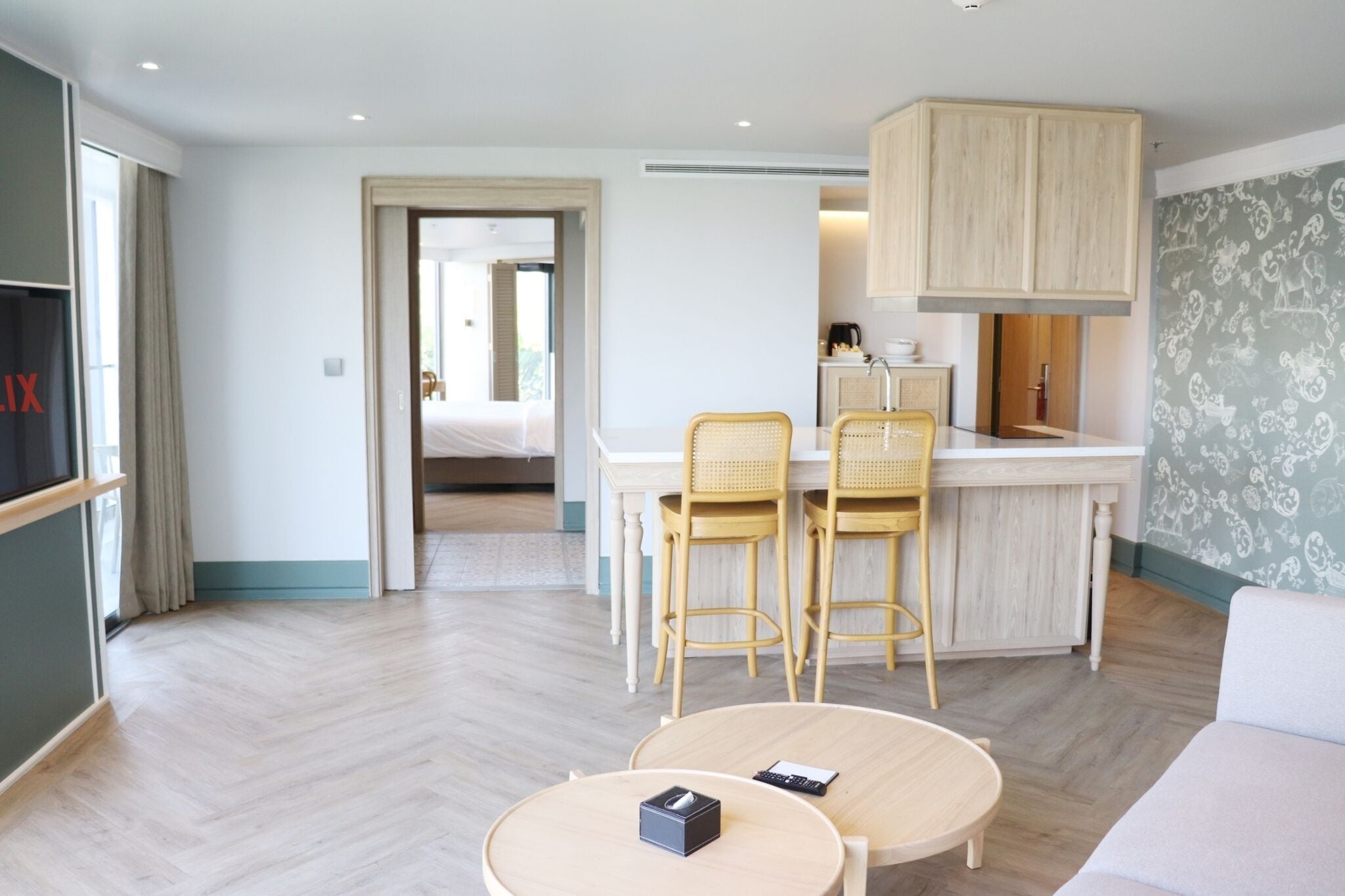 A modern hotel room with a kitchenette, a dining area with two chairs, a small round table, and a sofa.