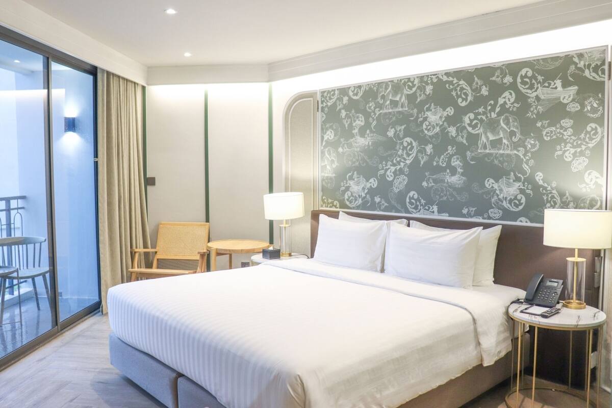 A hotel room with a large bed, two bedside tables with lamps, a chair, a small table, and a balcony with a view.