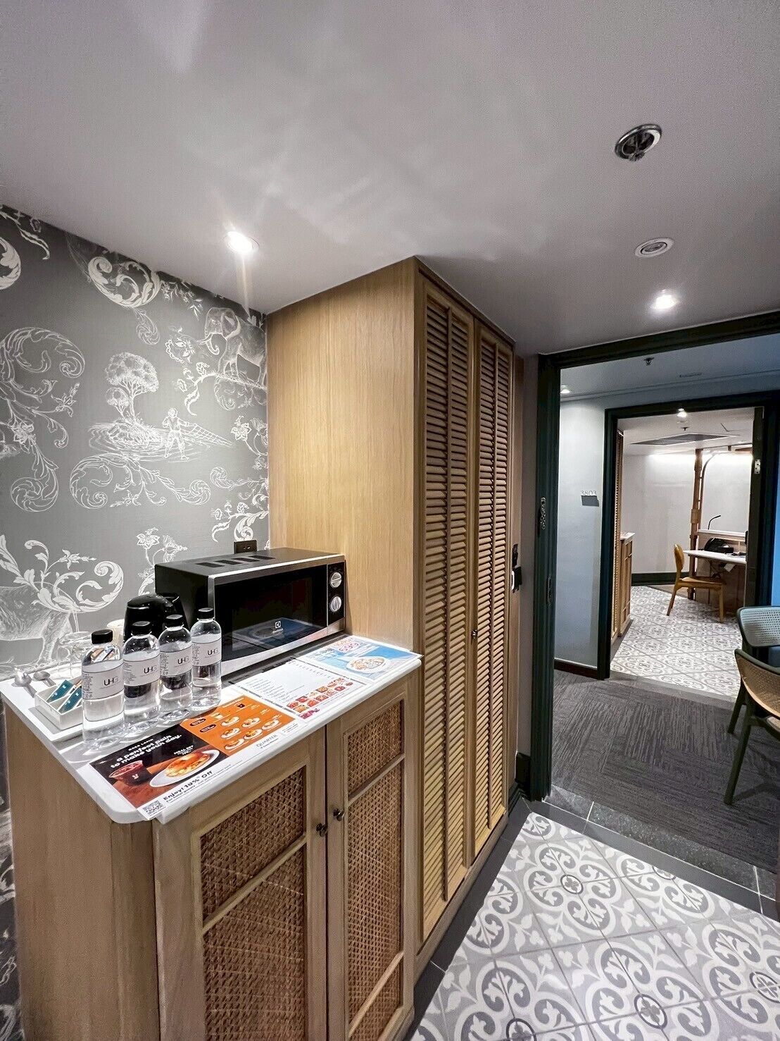 Een compacte hotelkamer met een kitchenette, een behang met patroon en uitzicht op de eetruimte.