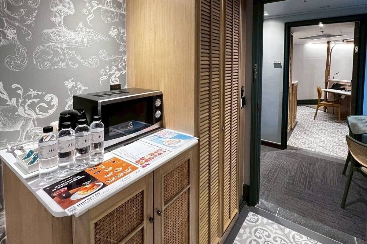 A compact hotel room with a kitchenette, a patterned wall, and a view into the dining area.