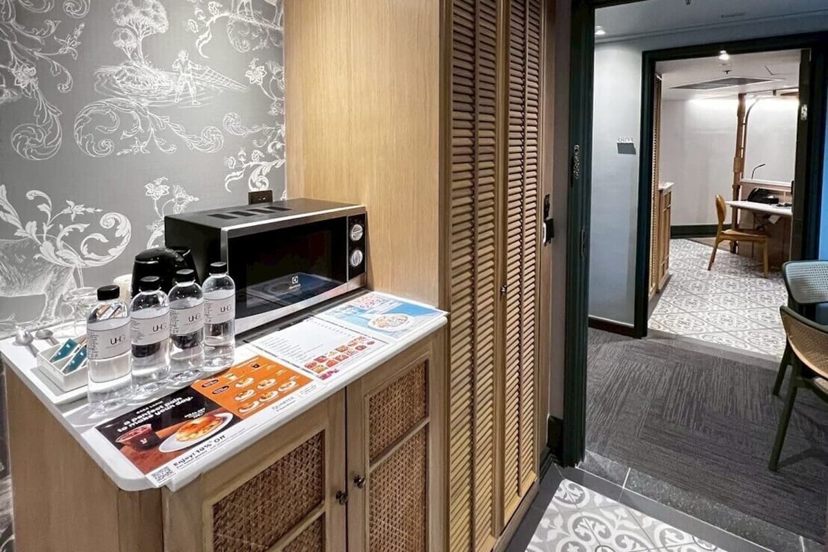 A compact hotel room with a kitchenette, a patterned wall, and a view into the dining area.