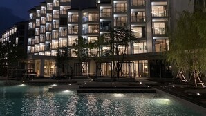 A modern hotel with multiple balconies, a swimming pool, and a well-lit facade. - The Quarter Chaophraya by UHG (Bangkok)