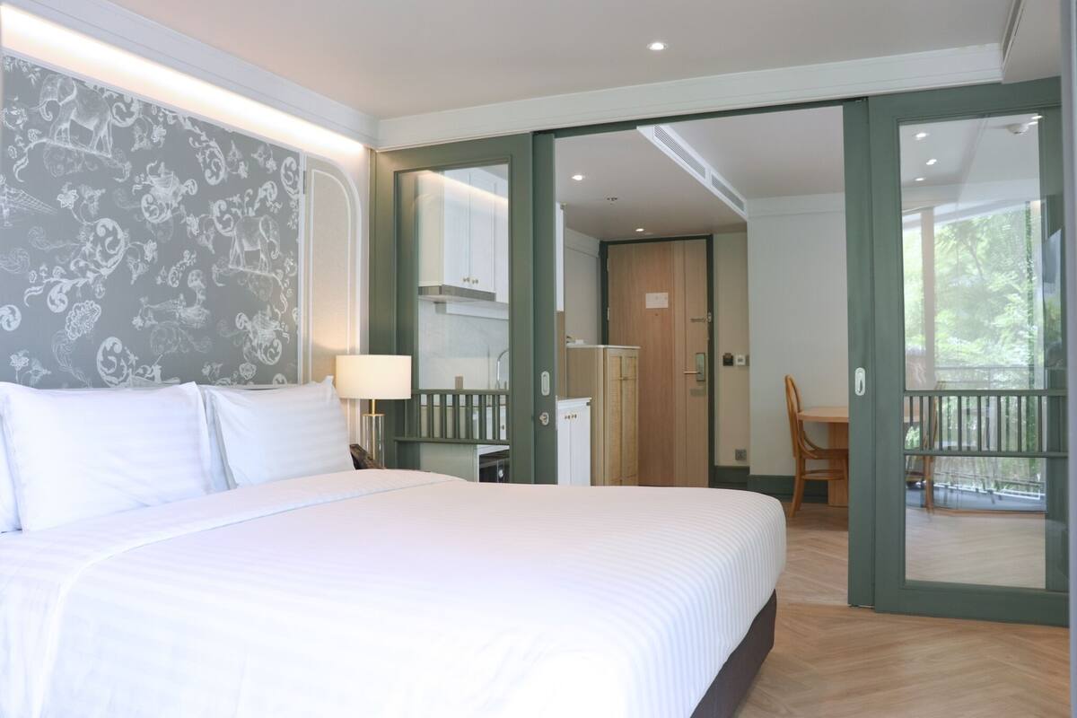 A hotel room with a large bed, a desk, a chair, and a balcony with a view.
