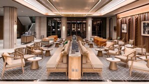 A spacious lobby with a central bar area, seating arrangements, and a modern ceiling design. - The Quarter Chaophraya by UHG (Bangkok)