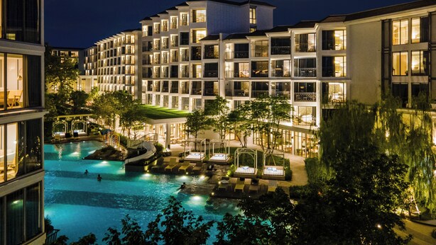 A multi-story hotel with a swimming pool, outdoor seating, and a well-lit facade. - The Quarter Chaophraya by UHG (Bangkok)