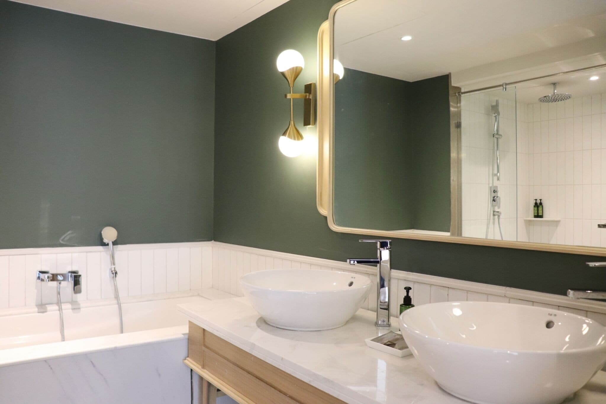 Un baño moderno con dos lavamanos blancos tipo isla, un espejo grande y una zona de ducha.