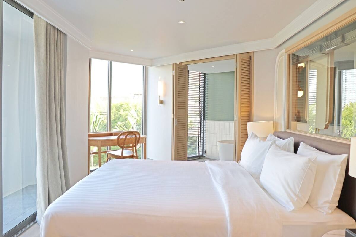 A hotel room with a large bed, a desk, a chair, and a balcony with a view.