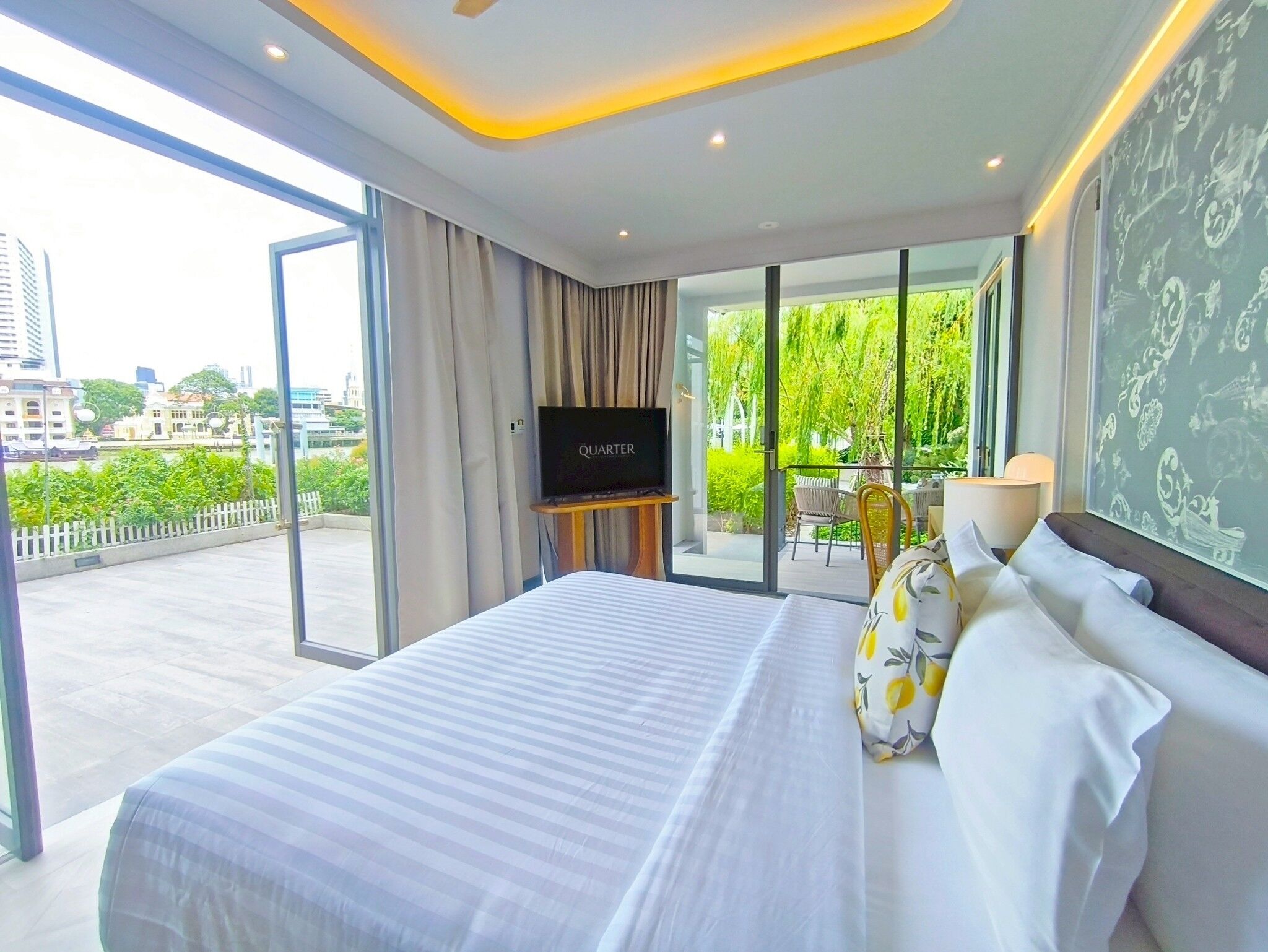 Habitación de hotel con una cama grande, televisión y vistas a zonas verdes y edificios.
