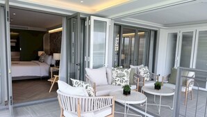 A modern hotel room with a bed, a sofa, a chair, a small table, and a sliding glass door leading to another room. - The Quarter Chaophraya by UHG (Bangkok)