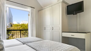 Un dormitorio con dos camas, televisor y balcón con cortinas.