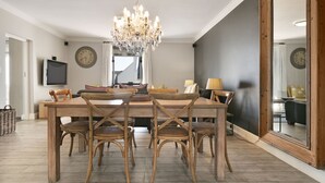 Comedor con mesa de madera, cuatro sillas, una araña y dos relojes de pared.