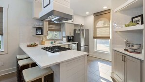 A modern kitchen with a central island, bar stools, a built-in oven, and a stainless steel refrigerator. - Coastal home w/ bikes & fenced yard (Santa Rosa Beach)