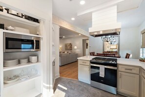 Enjoy cooking in the well-equipped kitchen with a central island, stove, and oven, adjacent to a dining area with a chandelier and large mirror.