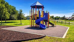 Un parque infantil con un tobogán azul, estructuras de juego amarillas y rojas, y un refugio de techo azul.