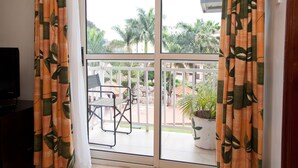 A balcony with a white railing, a table, and a chair. There is a potted plant on the balcony. - Mosa Court Apartments (Kampala)