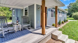 A covered porch with a wooden bench and a table, a small chair, and a bottle of wine. - Bear Walk Cottage in Black Mountain (Black Mountain)